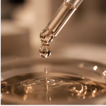 Una goccia di siero cade dal contagocce in una superficie d’olio dorato